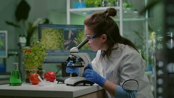 Portrait of biologist scientist in white coat working in expertise laboratory looking into microscope analyzing organic gmo leaf. Specialist researcher doing biochemistry experiment video