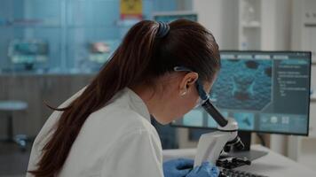 Woman examining dna sample on microscope tray in laboratory to analyze substance. Biochemistry specialist using magnifying glass lens on microscopic tool for research and development. video