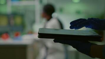 cientista investigador médico analisando genético mutação teste usando tábua enquanto dela colega digitando biológico perícia em computador dentro fundo. médico equipe trabalhando dentro microbiologia laboratório video