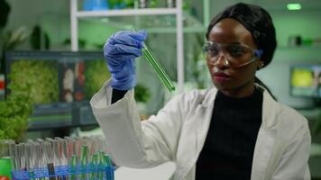African reseacher looking at test tube with green dna of sapling analyzing genetic mutation modified for microbiology experiment. Scientist working in agriculture laboratory developing eco environment video