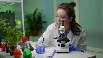 Biologist scientist looking at leaf sample using medical microscope while writing gmo expertise on notepad. Chemist examining biological discovery on plant working in pharmaceutical laboratory video