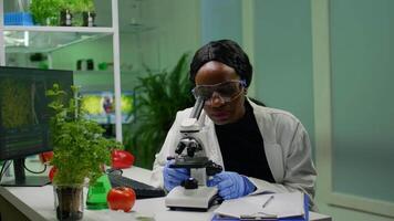 Biologist researcher scientist looking at leaf sample under medical microscope while writing biological expertise on notepad. Chemist examining biological discovery working in microbiology lab video