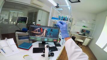POV of scientist looking at biological samples under microscope typing on pc. Team of chemists working in lab, examining virus evolution using high tech for scientific research of vaccine development. video