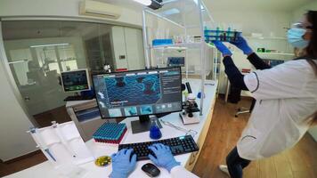 FPV of scientist holding blood sample from test tube analysing and typing on pc vaccine evolution. Team of doctors, viorolog researcher in professional lab working to discover medical treatment. video