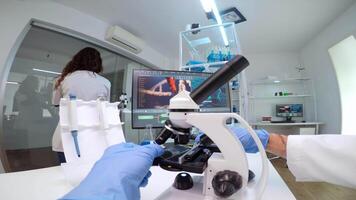 FPV of medical scientist looking under microscope, analyzes petri dish sample in equipped lab. Medical stuff examining vaccine development using high tech researching treatment against covid19 virus video