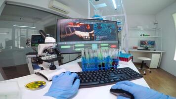 FPV of doctor chemist holding a flask of blue solution looking at it and typing on computer medical results. Scientists examining vaccine evolution in medical lab using high tech chemistry tools video