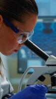 Vertical . Portrait of scientist looking under microscope in medical development laboratory, analyzing petri dish sample. Medicine, biotechnology research in advanced pharma lab, examining virus evolution video
