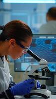 Vertical . Scientist looking at biological samples under microscope typing on pc. Team of chemists working in lab, examining virus evolution using high tech for scientific research of vaccine development. video