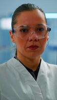 Vertical . Tired chemist doctor looking at camera sighing in modern equipped lab. Multiethnic team examining virus evolution using high tech and chemistry tools for scientific research, vaccine development. video