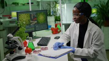 Scientists researchers working in biotechnology lab looking at vegan food and sapling analyzing genetic mutation writing biological expertise on notepad. Pharmaceutical researching biochemistry video