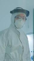 verticale . fatigué médecin dans protection costume contre covid-19 à la recherche épuisé à caméra derrière le verre mur travail dans danger zone. scientifique examiner virus évolution en utilisant haute technologie pour scientifique recherche video