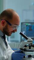 Vertical . Male scientist looking under microscope in medical development laboratory, entering data in computer. Specialists working on medicine, biotechnology research in advanced pharma lab video