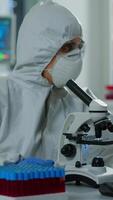 Vertical . Woman scientist in ppe suit working in lab using modern microscope with slides. Team of chemists researcher examining virus evolution using high tech for vaccine scientific research against covid19 video