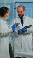 Vertical . Scientists coworkers using digital tablet working in medical research laboratory, analysing biochemicals samples, talking. Scientific lab for medicine, microbiology development with advanced equipment video