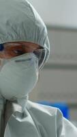 Vertical . Scientist in coverall doing research analysing liquid in tube at modern equipped laboratory. Biochemist examining vaccine evolution using high tech for treatment development against covid19 virus video