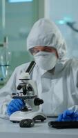 Vertical . Biologist doctor in coverall checking DNA sample on microscope typing on pc in equipped lab. Examining vaccine evolution in medical lab using high tech and chemistry tools for scientific research video