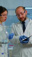 Vertical . Scientist team meeting and discusssing treatment results standing in research laboratory pointing on tablet. Stuff examining vaccine development against covid19 virus using high tech for researching. video