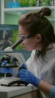 Vertical . Portrait of biologist scientist in white coat working in expertise laboratory looking into microscope analyzing organic gmo leaf. Specialist researcher doing biochemistry experiment video