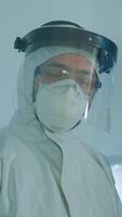 Vertical . Microbiologist in ppe suit standing in laboratory looking at camera behind the glass wall in equipped lab. Doctor examining virus evolution using high tech and chemistry tools for vaccine development video