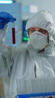 Vertical . Neurologist with ppe suit working at vaccine development analysing blood sample in equipped laboratory typing on pc. Team examining virus evolution using high tech for research in treatment for covid19 video