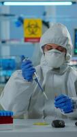 Vertical . Science technician in ppe suit using micropipette and petri dish working in research laboratory analysing blood sample. Team examining virus evolution for vaccine development against covid19 video
