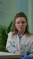Vertical . Pov of botanist woman in white coat listening chemists team during online videocall meeting while sitting in pharmaceutical lab. Specialists team researching genetic mutation developing dna GMO biology test video