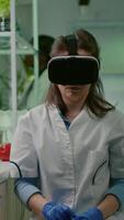 Vertical . Scientist woman researcher wearing virtual reality headset developing new biotechnology for biological experiment. Medical team working in microbiology laboratory analyzing dna test video
