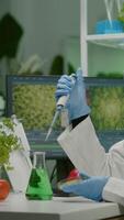 Vertical . Biologist scientist african woman researcher taking genetic solution from test tube with micropipette putting in petri dish analyzing gmo of sapling working in biological laboratory. video
