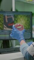 vertical . químico mujer analizando vegano carne de vaca carne para bioquímica experimento. biólogo investigador examinando comida genéticamente modificado utilizando químico sustancia mecanografía biológico pericia en computadora video