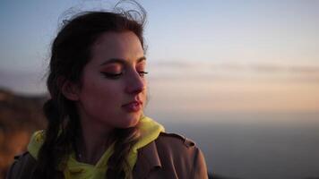Closeup portrait of sensual young brunette woman, looking up in sky, happily outdoors isolated at blurry sea background natural bokeh in soft warm sunset backlight. video