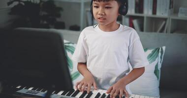 Handheld shot, Creative asian boy wearing headphone with artistic skills taking music lessons online during a video call and playing the piano at home. Music, hobby and lifestyle concepts.