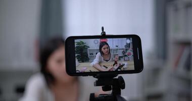 handheld schot, detailopname telefoon visie, mooi Aziatisch vrouw blogger is tonen hoe naar maken omhoog en gebruik cosmetica. in voorkant van de smartphone naar Vermelding vlog video. influencer en schoonheidsmiddelen concepten. video