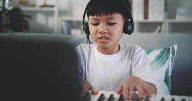 Handheld shot, Creative asian boy wearing headphone with artistic skills taking music lessons online during a video call and playing the piano at home. Music, hobby and lifestyle concepts.