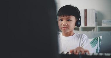 Dolly shot, Creative asian boy wearing headphone with artistic skills taking music lessons online during a video call and playing the piano at home. Music, hobby and lifestyle concepts.