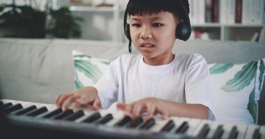 Handheld shot, Creative asian boy wearing headphone with artistic skills taking music lessons online during a video call and playing the piano at home. Music, hobby and lifestyle concepts.