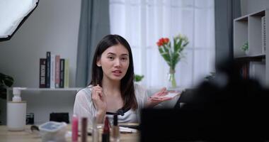 Footage of Beautiful asian woman blogger is showing how to makeup and use cosmetics. In front of the camera to record vlog video live streaming at home. Influencer and cosmetics concepts.