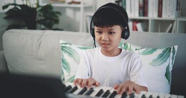 Handheld shot, Creative asian boy wearing headphone with artistic skills taking music lessons online during a video call and playing the piano at home. Music, hobby and lifestyle concepts.