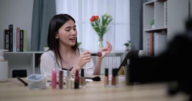 Handheld shot, Beautiful asian woman blogger is showing how to makeup and use cosmetics. In front of the camera to record vlog video live streaming at home. Influencer and cosmetics concepts.