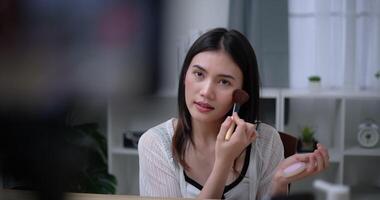Handheld shot, Beautiful asian woman blogger is showing how to makeup and use cosmetics. In front of the smartphone to record vlog video live streaming at home. Influencer and cosmetics concepts.