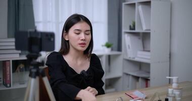 Handheld shot, Beautiful asian woman blogger is showing how to makeup and use cosmetics. In front of the smartphone to record vlog video live streaming at home. Influencer and cosmetics concepts.