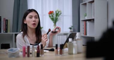 Footage of Beautiful asian woman blogger is showing how to makeup and use cosmetics. In front of the camera to record vlog video live streaming at home. Influencer and cosmetics concepts.