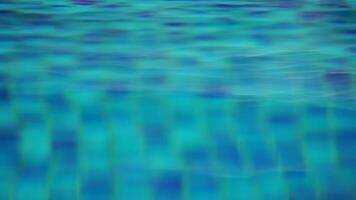 Pool water background with wavy clear fresh water. Calm rest on sunny day. Abstract reflections on the surface of the water with texture of bright blue pool tiles. Turquoise water surface. Slow motion video