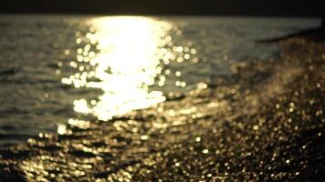 Blurred golden sea at sunset with shifting focus and bokeh effect. Sun reflects and sparkles on waves, illuminating golden sea. Holiday recreation concept. Abstract nautical summer ocean sunset nature video