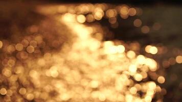 Abstract sea summer ocean sunset nature bokeh background. Small waves on azure water surface in motion blur with golden bokeh lights from sun. Holiday, vacation and recreational concept. Slow motion video