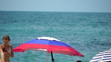 white blue red colored beach umbrellas or parasols against blue sea during a sunny day on a beach. Symbol of vacations, relax, summer. Colorful umbrellas from the sun stand on the beach. Slow motion. video