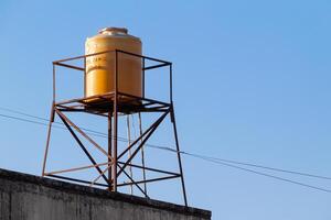 yellow plastic water tank tower on the roof with a clear sky in the background photo