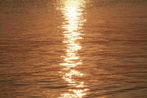 Calm ocean waves with golden light reflections from the rising sun photo