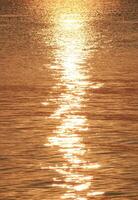 Calm ocean waves with golden light reflections from the rising sun photo