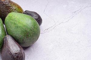 Avocados whole fruit are placed on a gray stone background with copy space for text. Close-up photo. Concept of healthy fruits photo