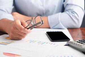 Close-up of hand holding a glasses reviewing the chart, graph report and calculating on the calculator for planning next step of the business. Space for text. Business, finance, and planning concept photo